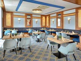 Einblick in den Restaurantraum mit hellblauen Samtstühlen an gedeckten Tischen 