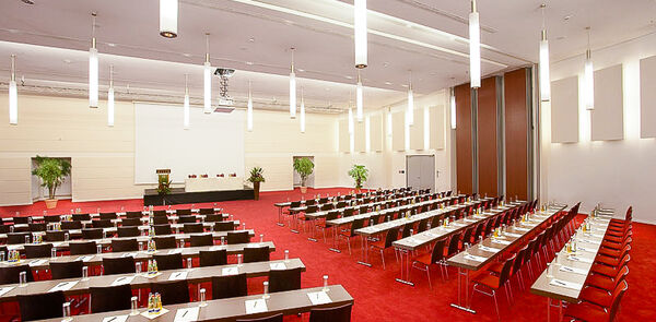 Zahlreiche Tischreihen mit Stühlen im Tagungsraum mit rotem Teppichboden im Tagungshotel in Niederbayern