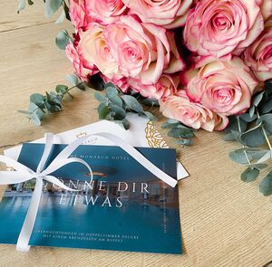 Gutscheine für das The Monarch Hotel in Bad Gögging auf einem Tisch neben einem Strauß Rosen 