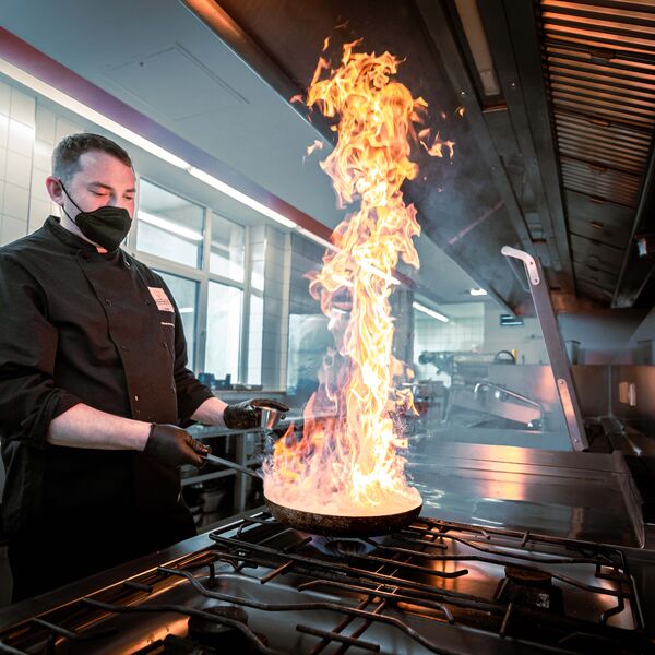 Koch brät mit einer Flamme in der Pfanne 